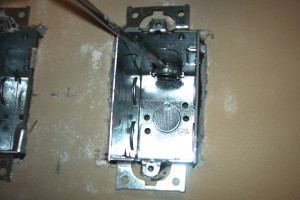 Mientras sostiene la caja eléctrica, deslice aquella dentro del orificio abierto en el drywall